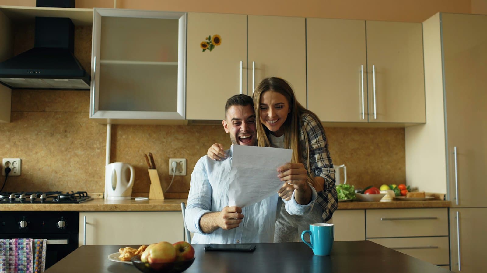 A couple at their kitchen table smiles with excitement while reading a letter together.
