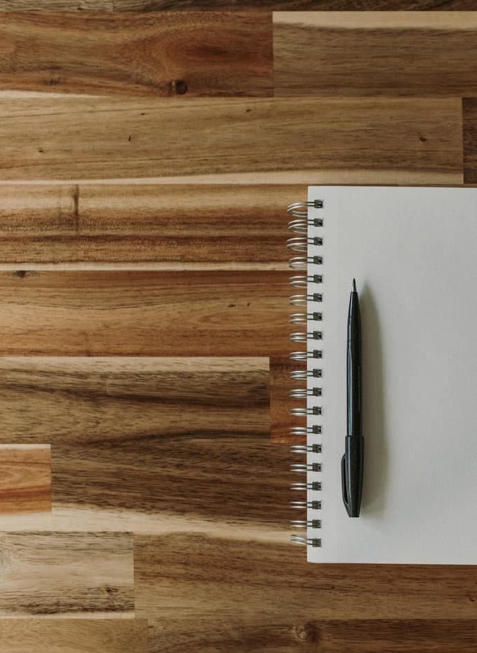 A notepad, a pen and a cup of coffee on a wooden table.