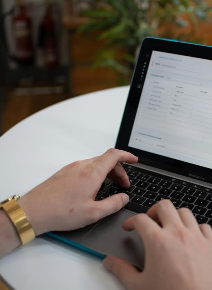 Hands typing on a laptop with a spreadsheet on the screen.