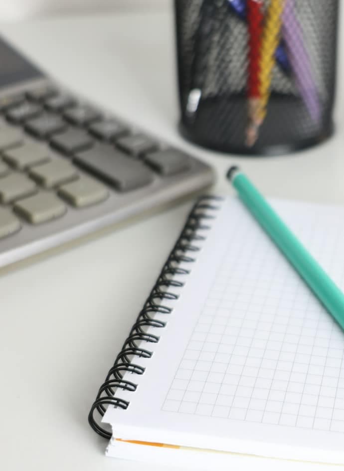 A desk with a calculator, notebook, pencil and a plant.